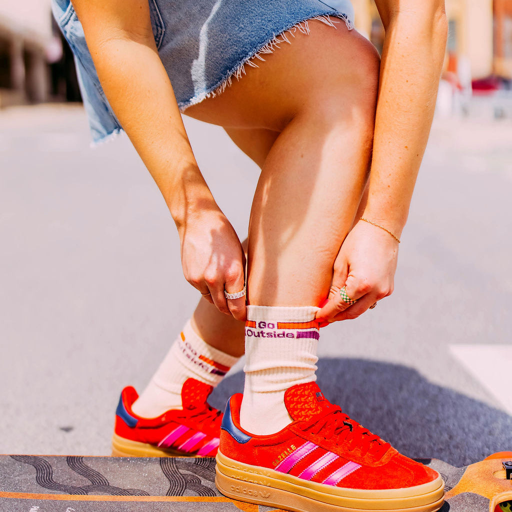 Go Outside Socks, cream striped Go Outside socks worn with red sneakers by a model stepping onto a skateboard