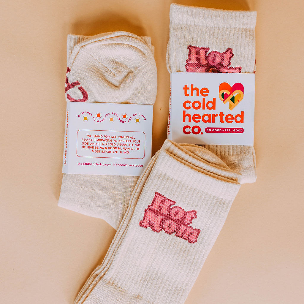Hot Mom Socks, cream crew socks with pink Hot Mom lettering, two pairs in Cold Hearted Co. bands on a peach backdrop