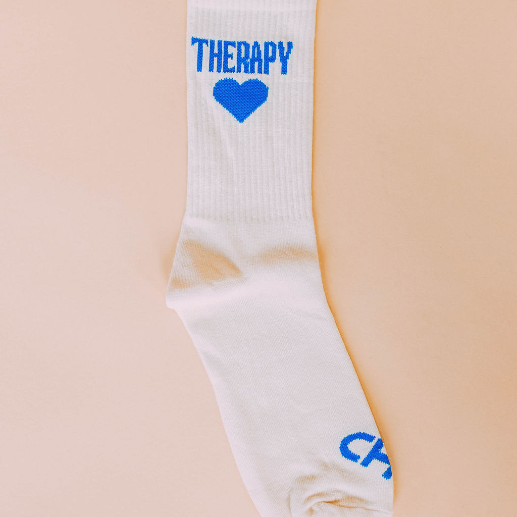 Therapy Socks, single cream crew sock with bright blue Therapy lettering and a blue heart on a peach background