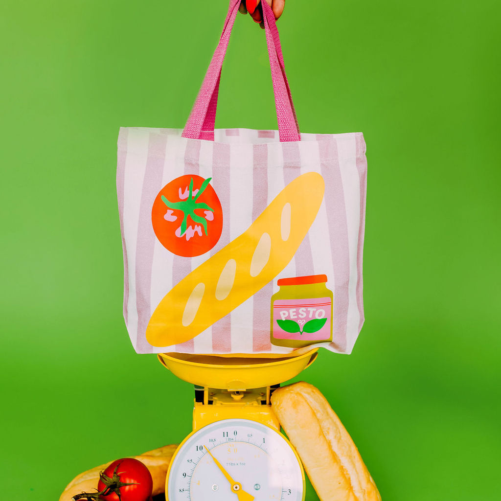 Pesto Baguette Market Tote, pink striped tote with a baguette, tomato and pesto jar held over a scale with bread