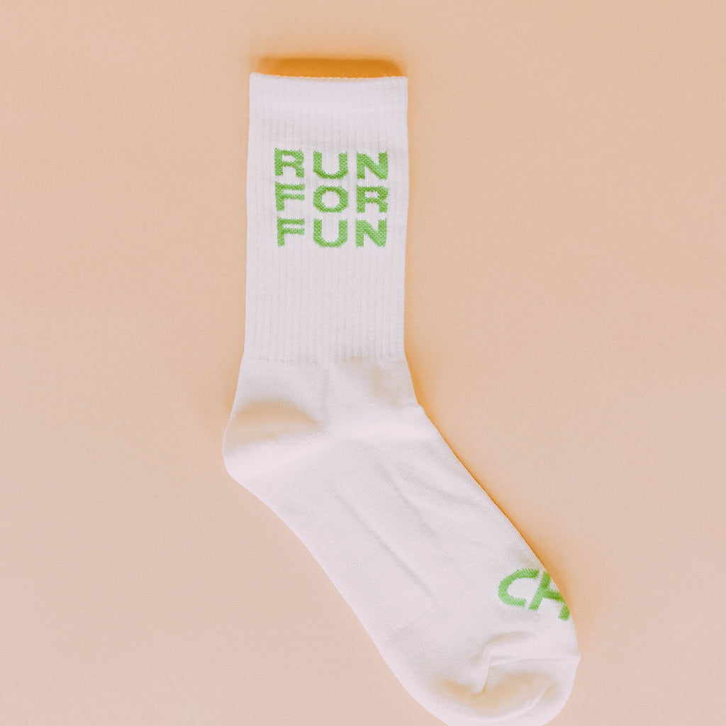 Run For Fun Socks, single cream crew sock with green Run For Fun block lettering, flat lay on peach background
