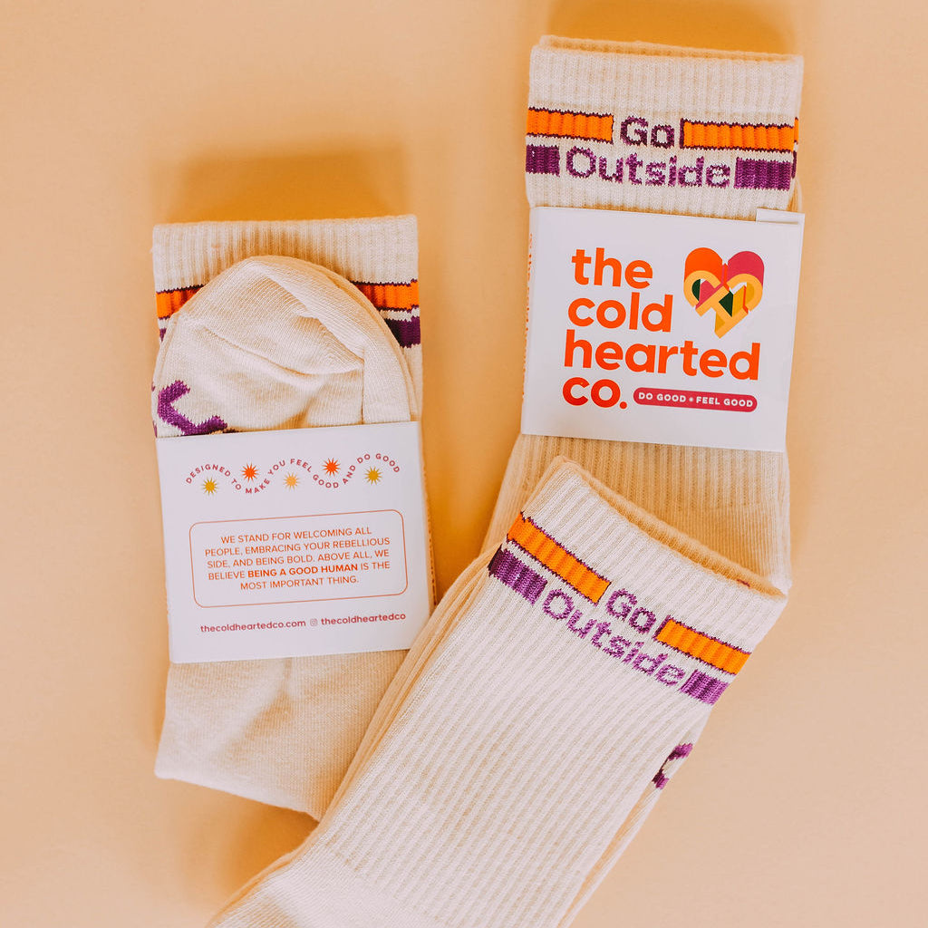 Go Outside Socks, cream socks with orange and purple stripes and Go Outside text plus brand packaging, flat lay