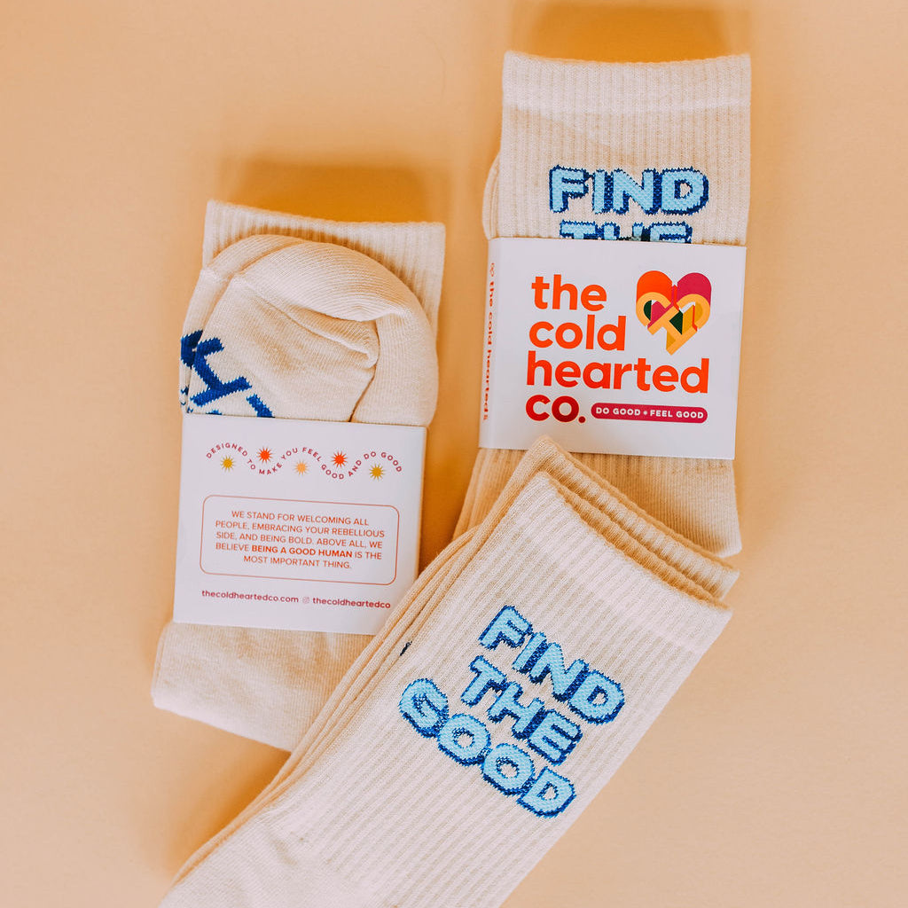 Find The Good Socks, cream socks with blue Find The Good block lettering and brand packaging, flat lay on peach