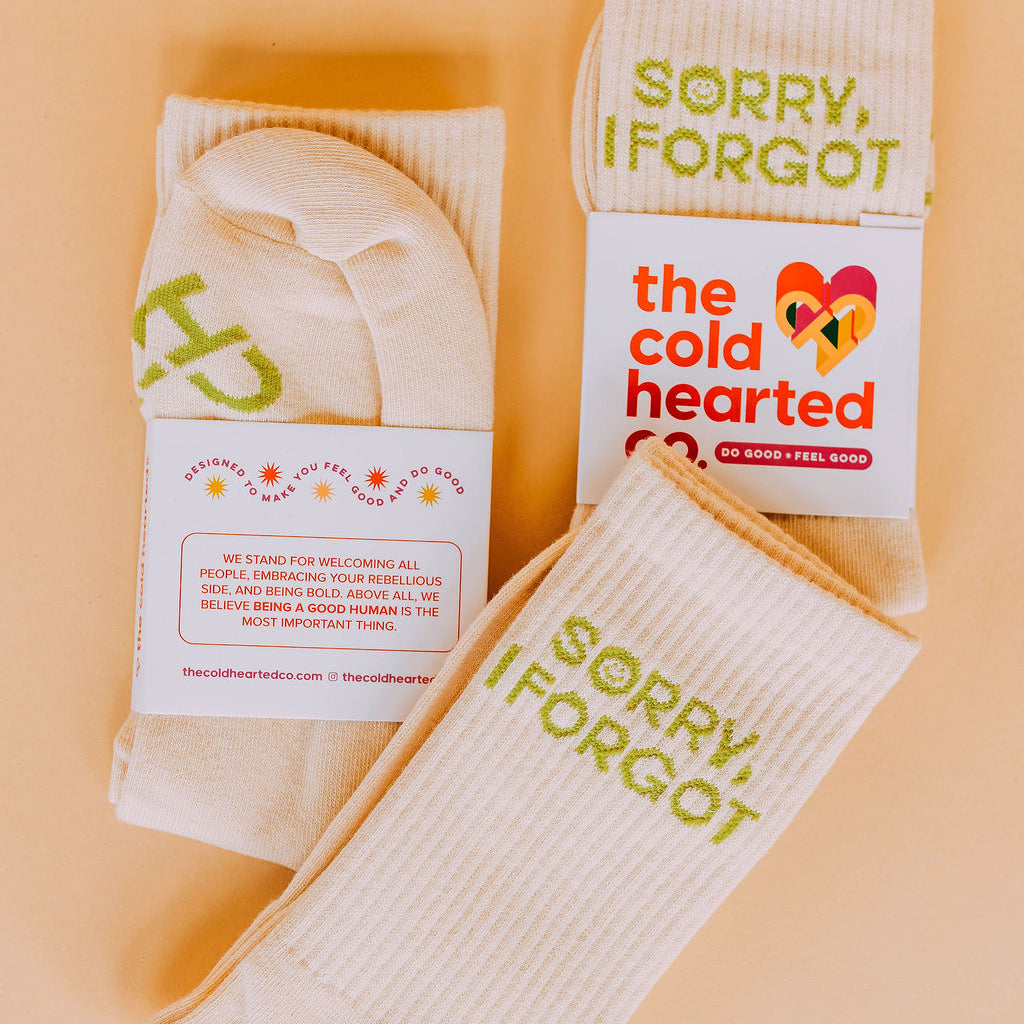 Sorry I Forgot Socks, cream socks with green Sorry, I Forgot text and brand packaging, flat lay on peach