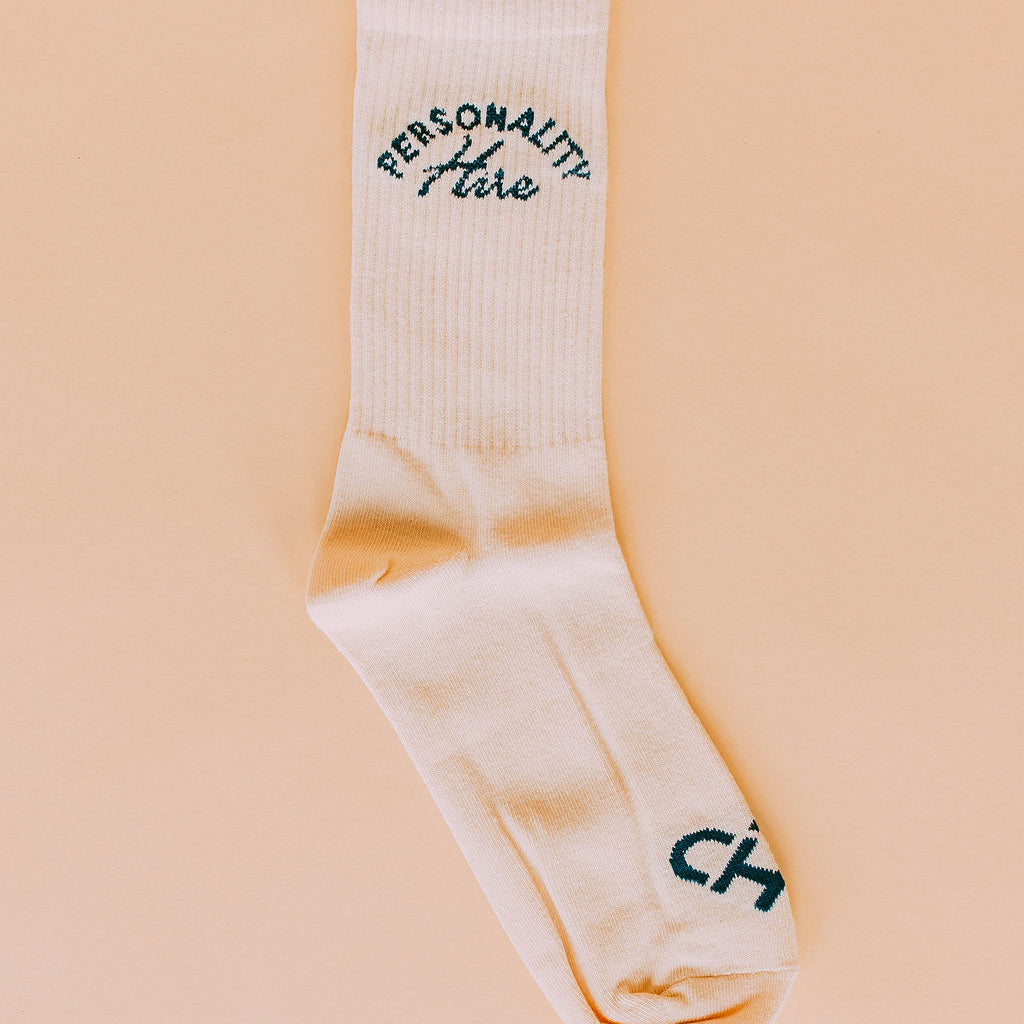 Personality Hire Socks, cream crew sock with dark green arched Personality Hire lettering laid on a peach background