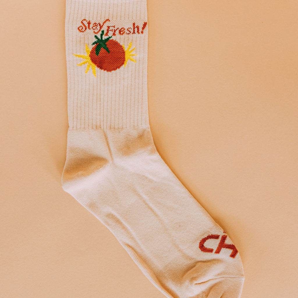 Stay Fresh Tomato Crew Socks, single cream crew sock with a red tomato and Stay Fresh text, flat lay on peach