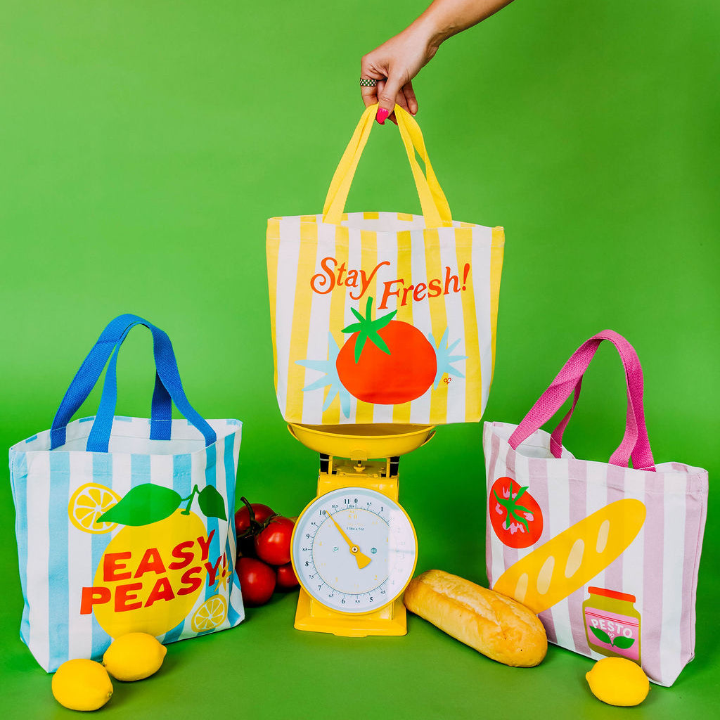 Pesto Baguette Market Tote, pink striped tote shown with lemon and tomato totes around a yellow scale on green