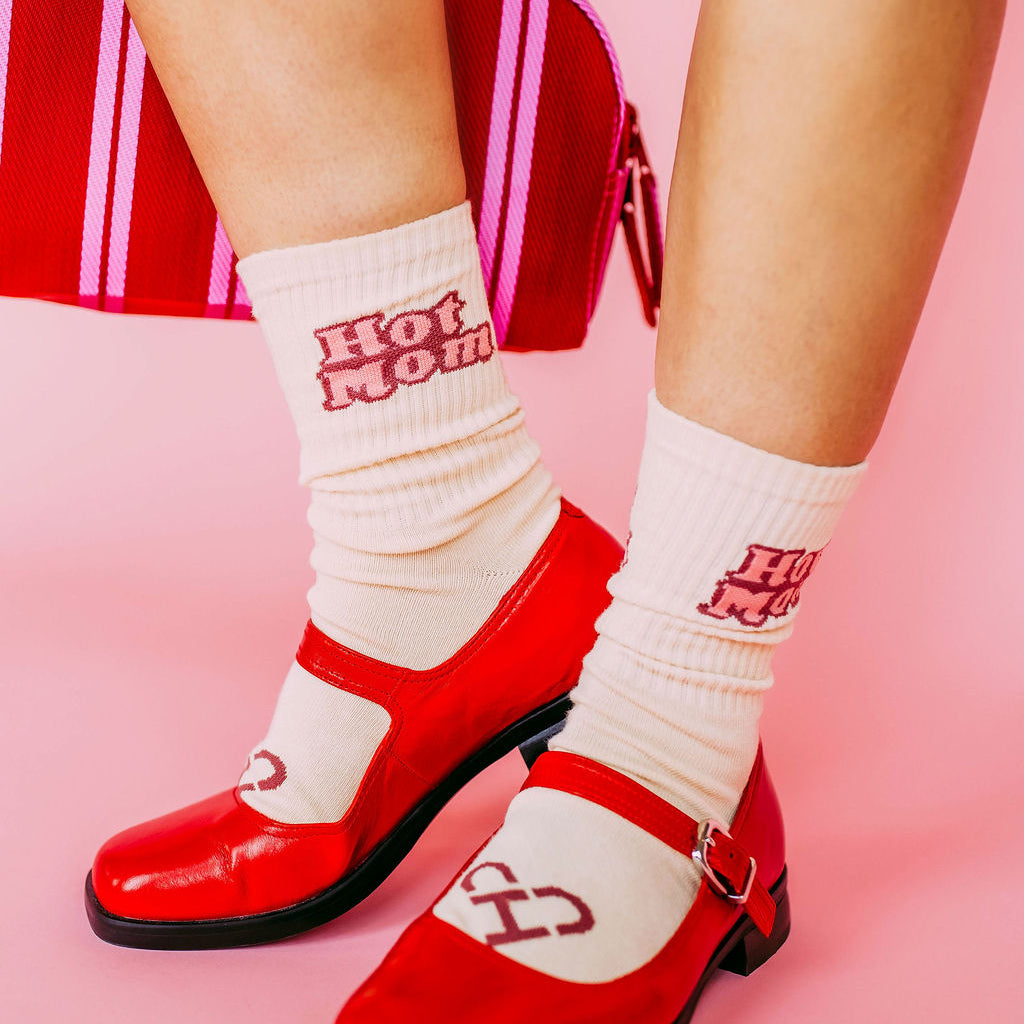 Hot Mom Socks worn with red Mary Jane shoes on a pink backdrop, cream socks with red Hot Mom lettering