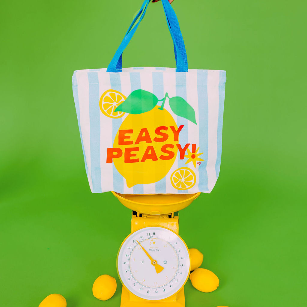 Easy Peasy Lemon Market Tote, blue striped tote with a lemon and red Easy Peasy text held above a yellow scale