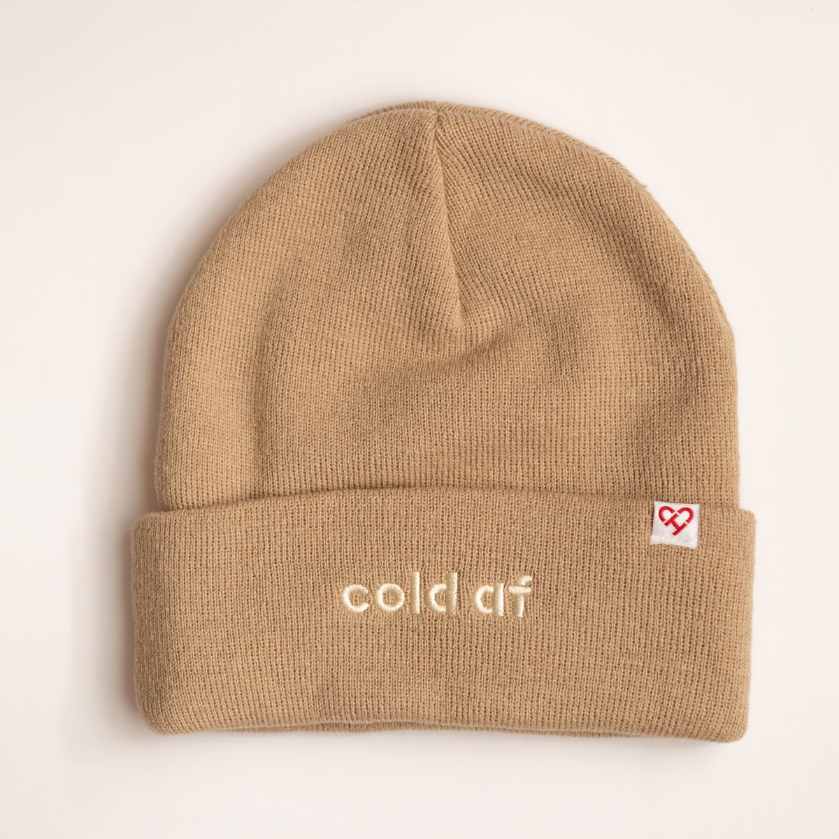 Cold AF Beanie, tan cuffed knit beanie with cream embroidered cold af lettering and a small red heart logo tag