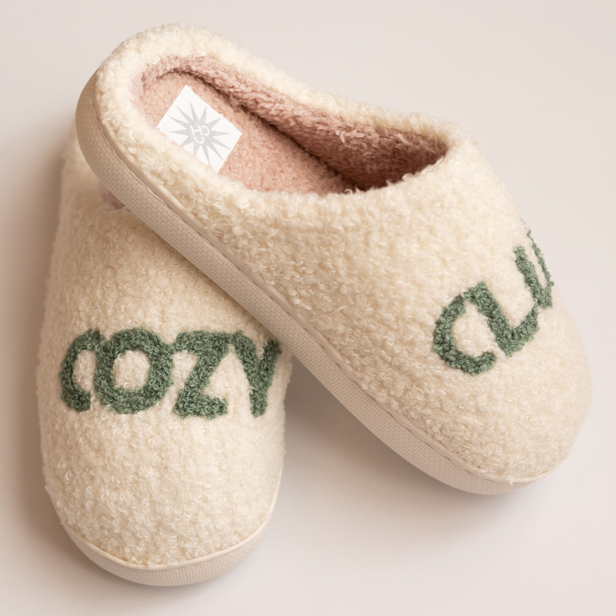 Cozy Club Slippers, stacked pair of cream sherpa slippers with green tufted Cozy Club lettering and pink lining