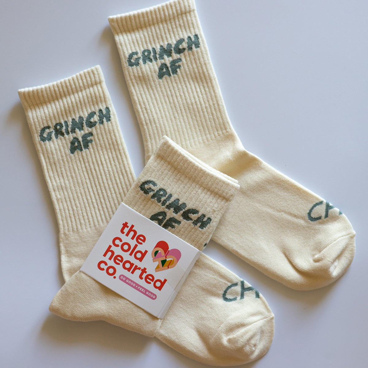 Grinch AF Socks, cream crew socks with green Grinch AF lettering, one pair in a Cold Hearted Co. band, flat lay