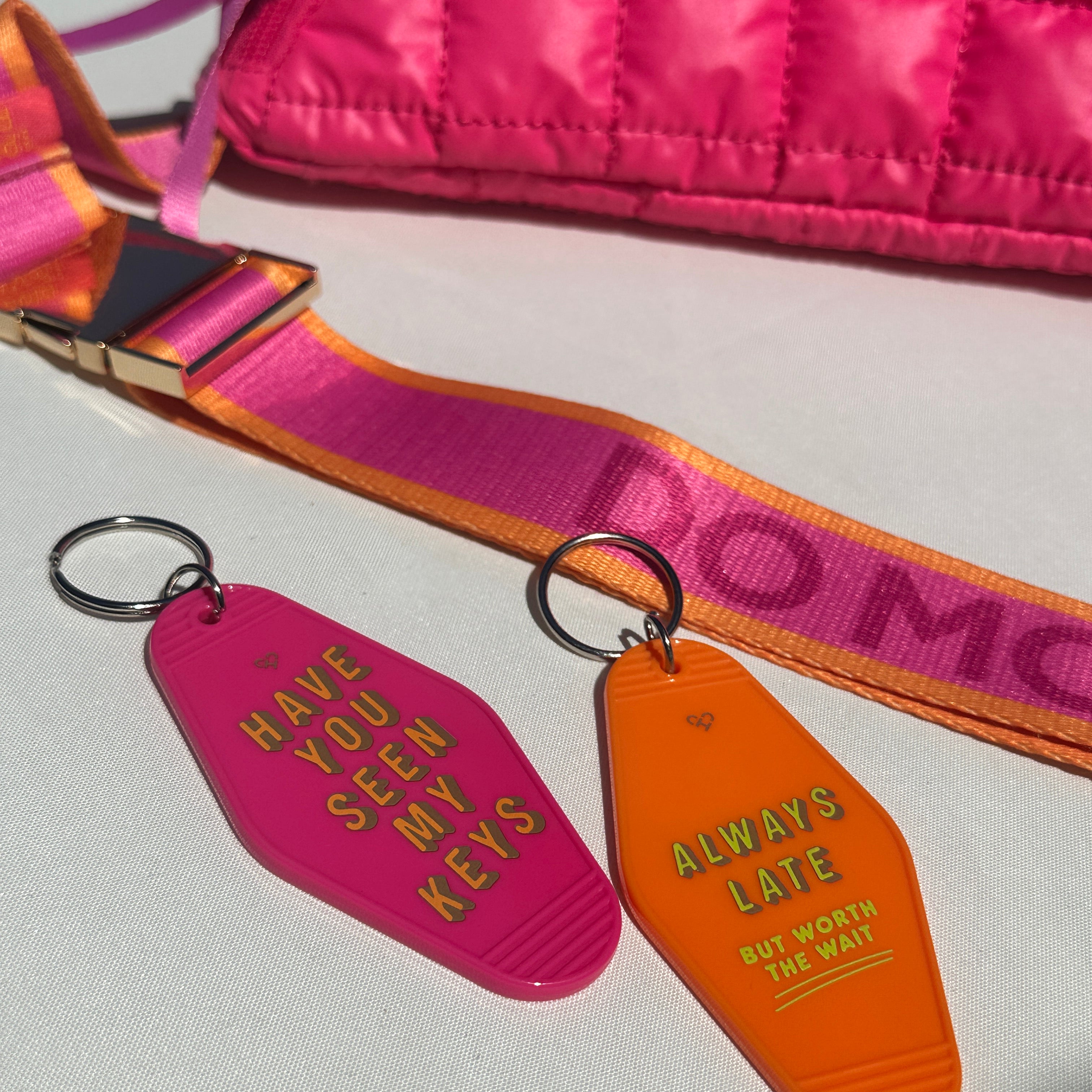 Have You Seen My Keys and Always Late motel keychains in pink and orange beside a pink quilted Do More Good bag