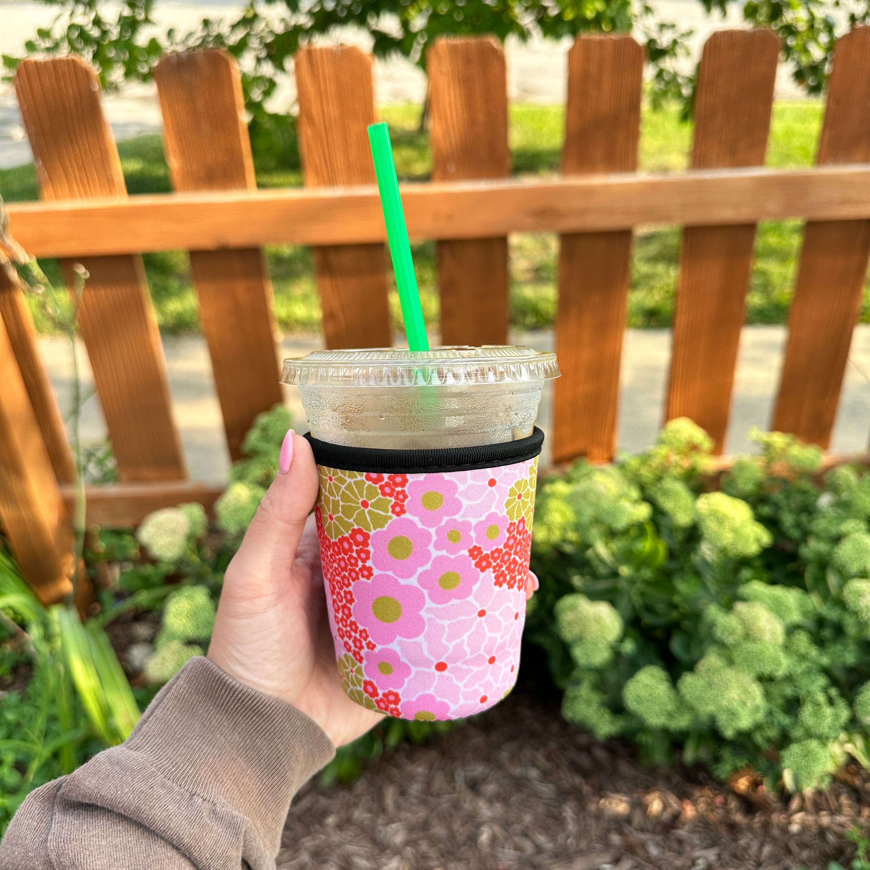 Floral Iced Coffee Sleeve, pink flower print sleeve on an iced coffee with green straw held by a wooden fence