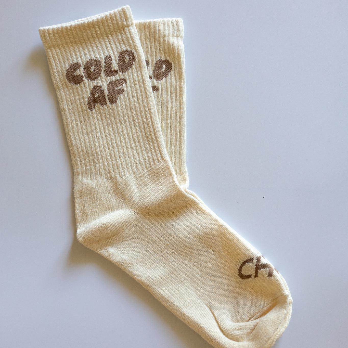 Cold AF Socks, pair of cream ribbed crew socks with brown Cold AF lettering on the cuff laid flat on white