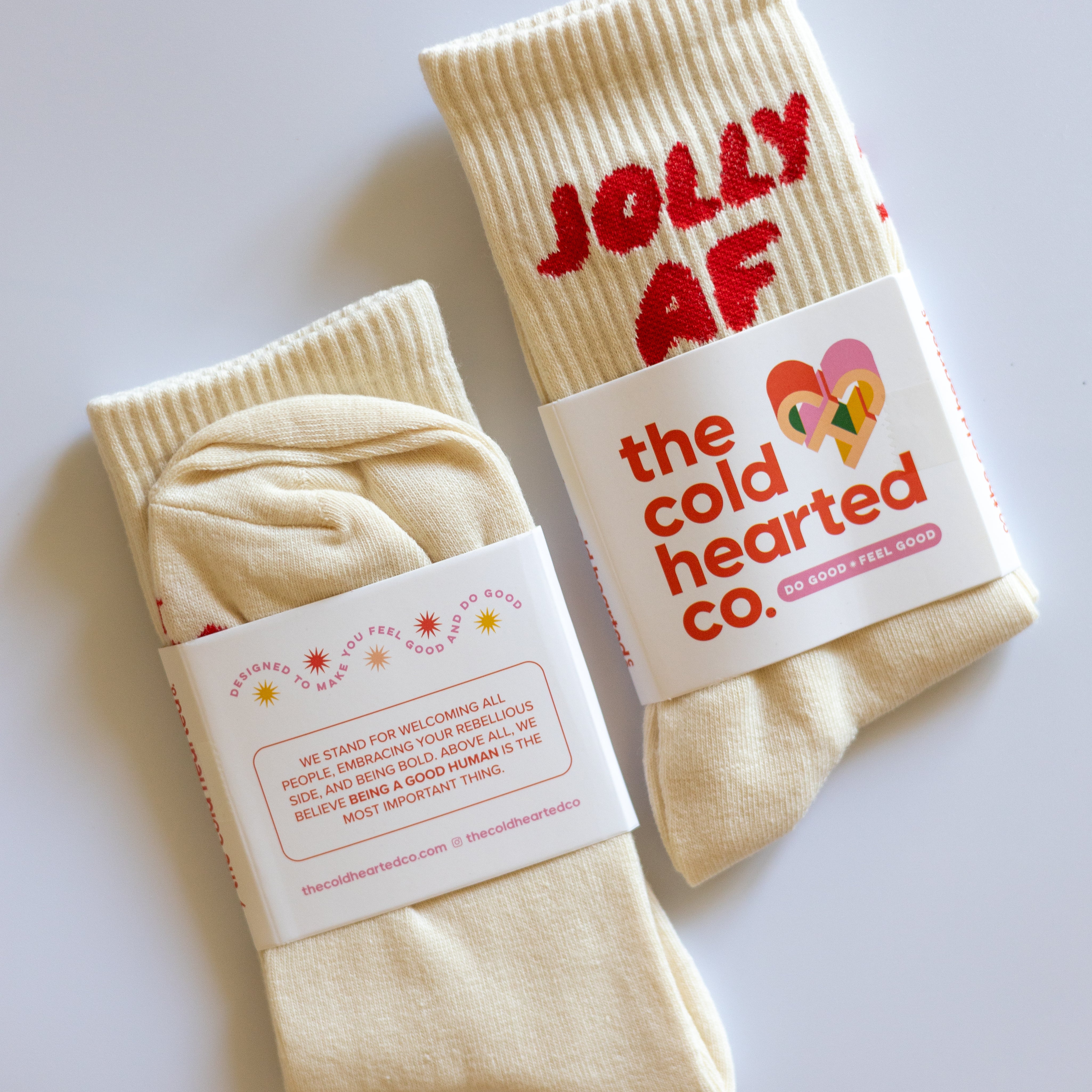 Jolly AF Socks, cream crew socks with red Jolly AF lettering in Cold Hearted Co. packaging bands on a white surface