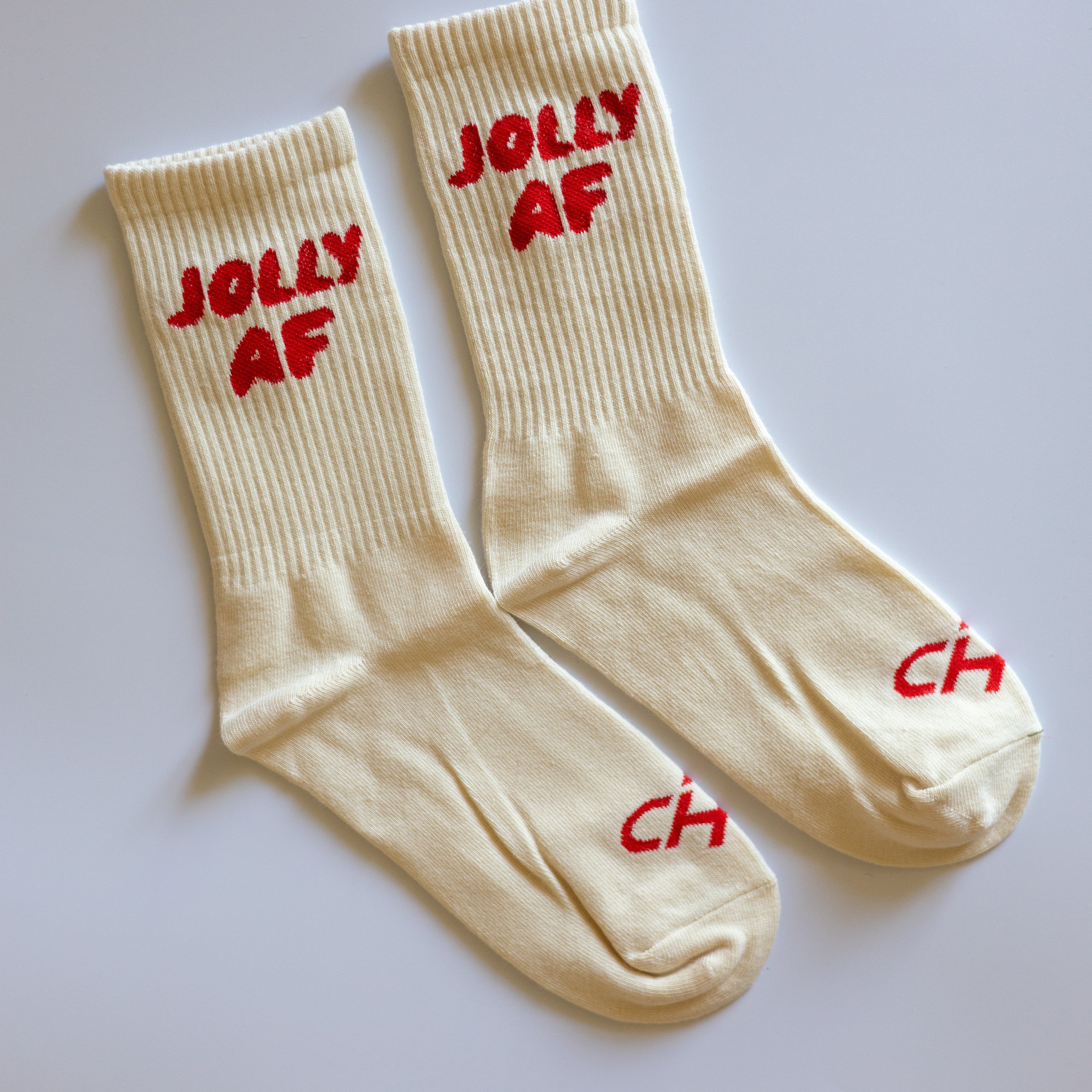 Jolly AF Socks, pair of cream ribbed crew socks with red Jolly AF lettering and red CH on the toes, laid flat