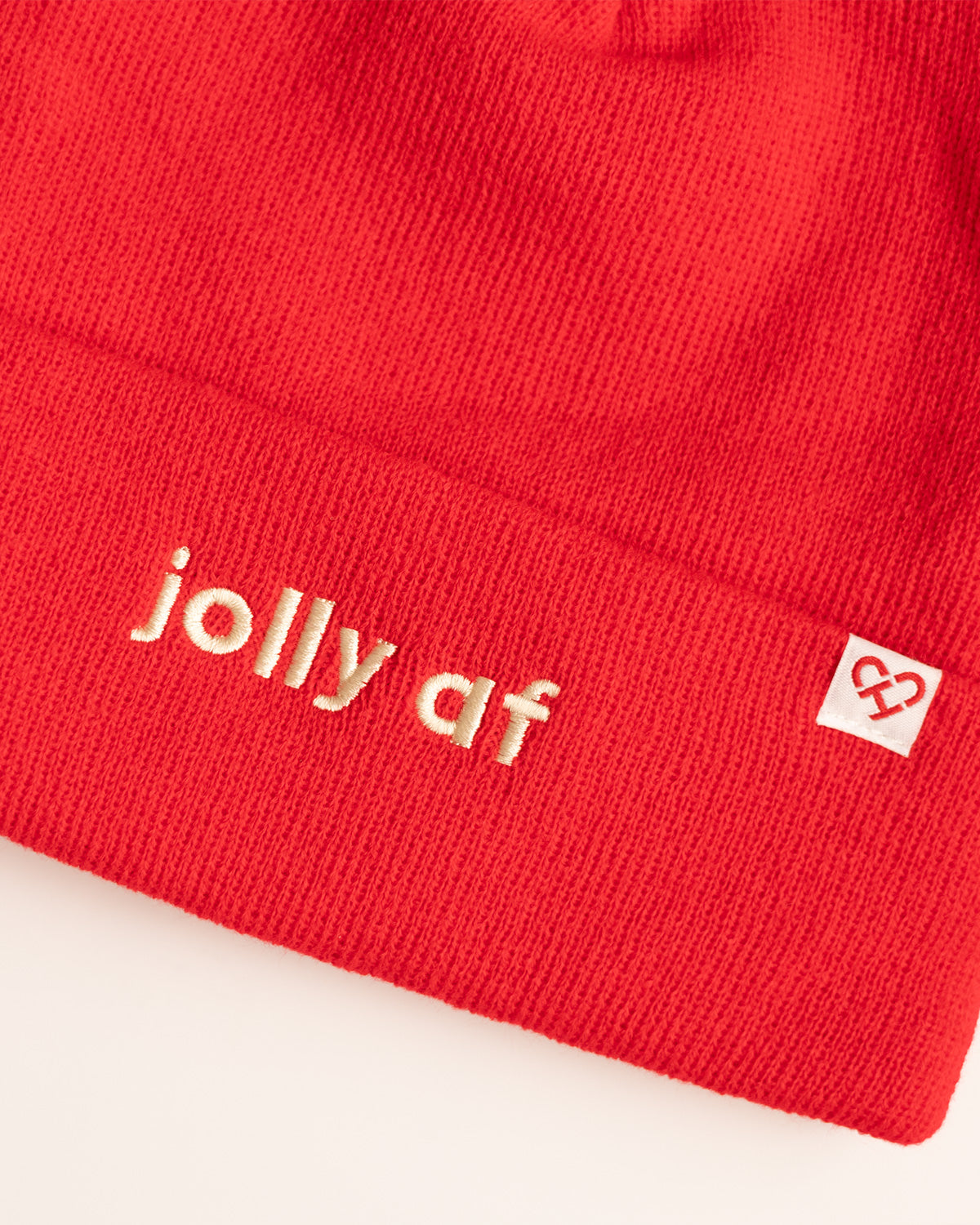 Jolly AF Beanie, close up of red knit cuff with cream embroidered jolly af text and a white heart logo tag