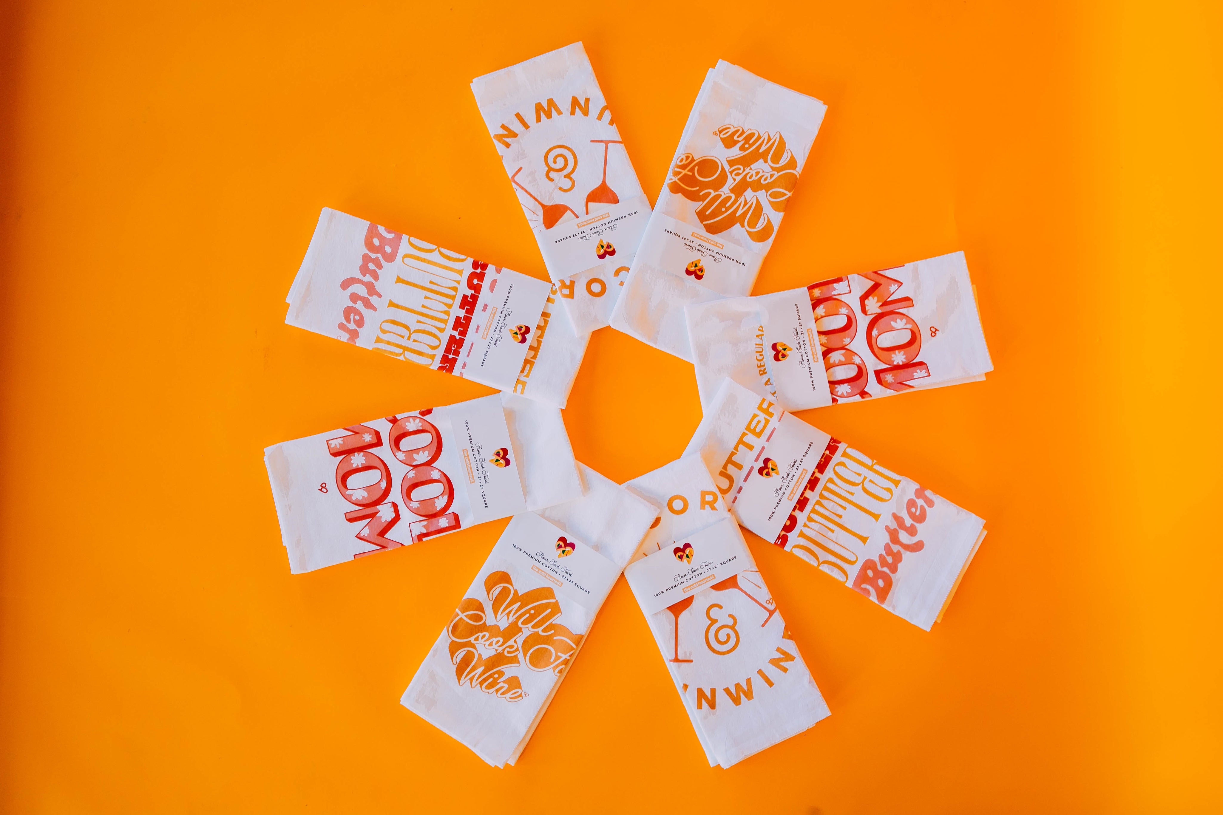 Butter Flour Sack Towel, flat lay of folded white tea towels with red and gold prints on bright orange
