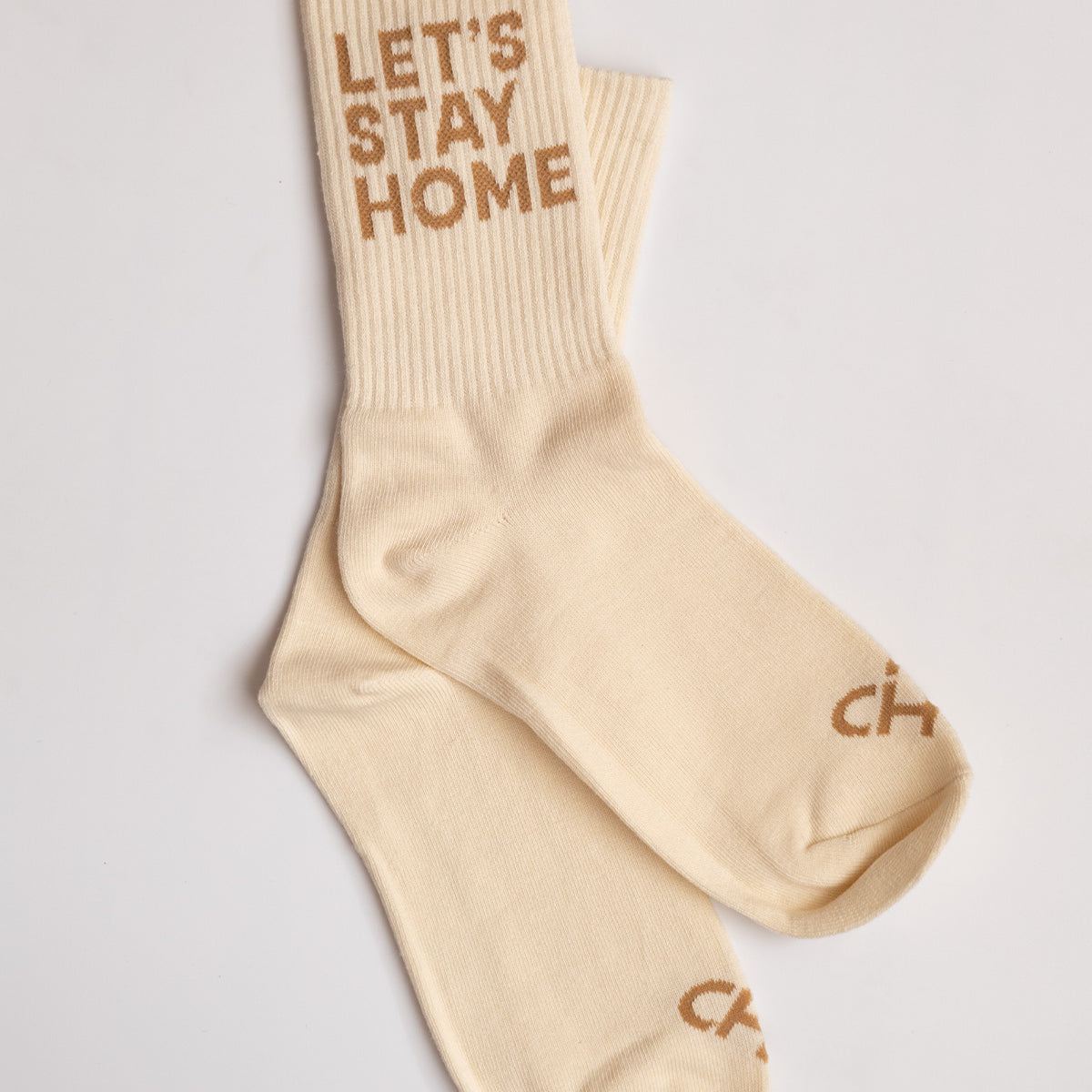 Let's Stay Home Socks, cream ribbed crew socks with tan Let's Stay Home lettering on the cuff, flat lay