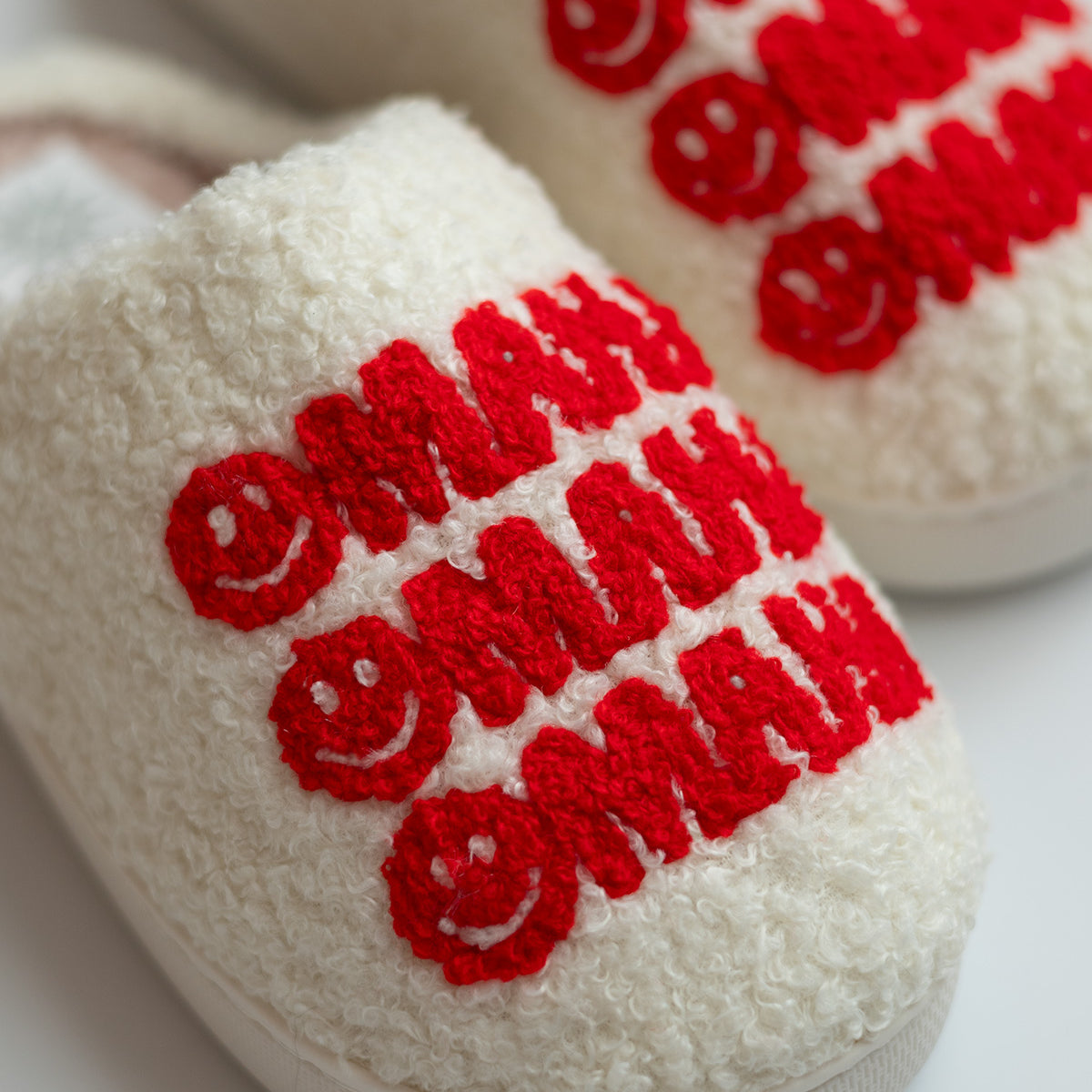 DOORBUSTER Omaha Smiley Slippers, close up of cream fuzzy slipper toe with red tufted smiley Omaha lettering