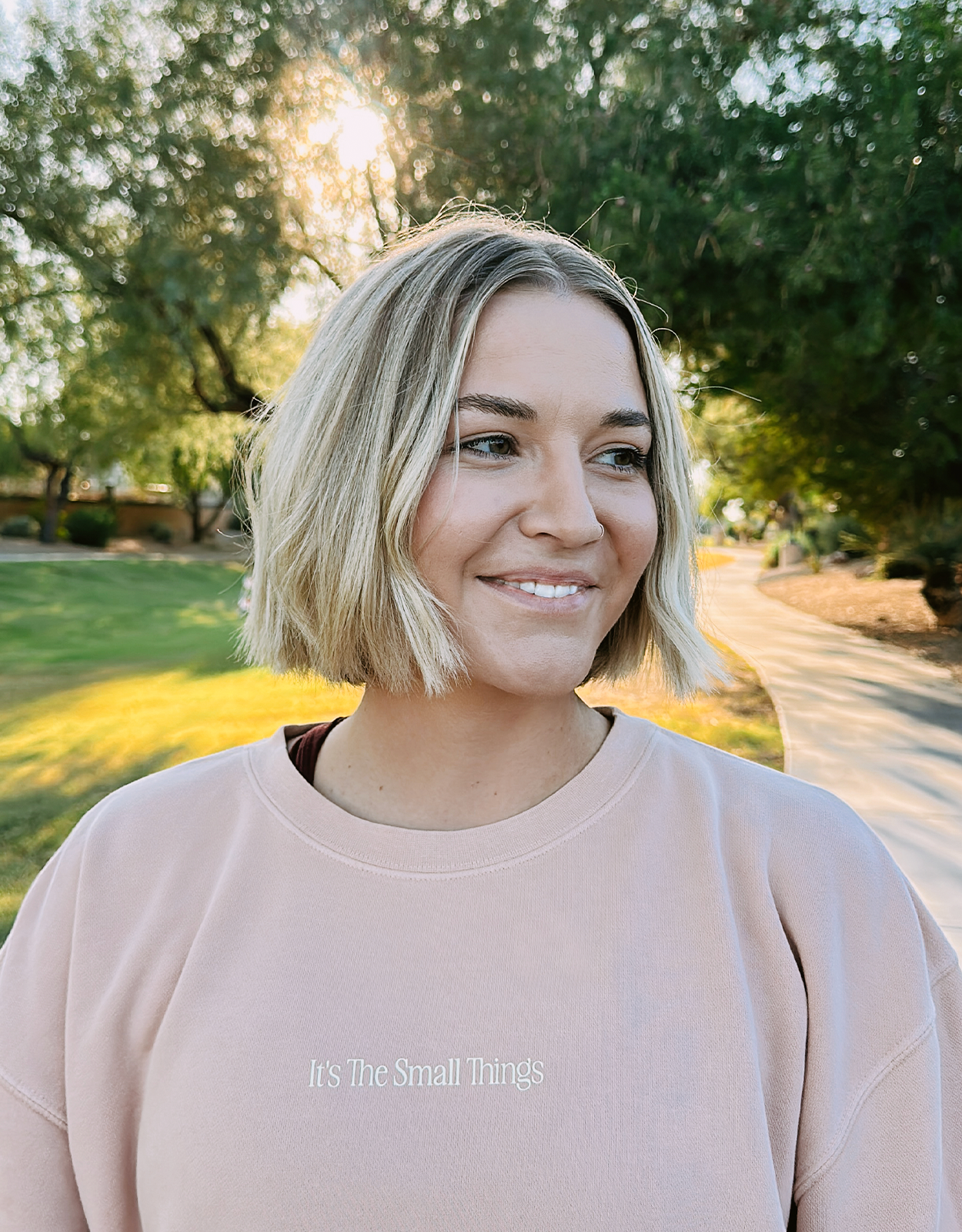 Appreciate Small Things Crew, smiling model outdoors in a peach crewneck with It's The Small Things chest text