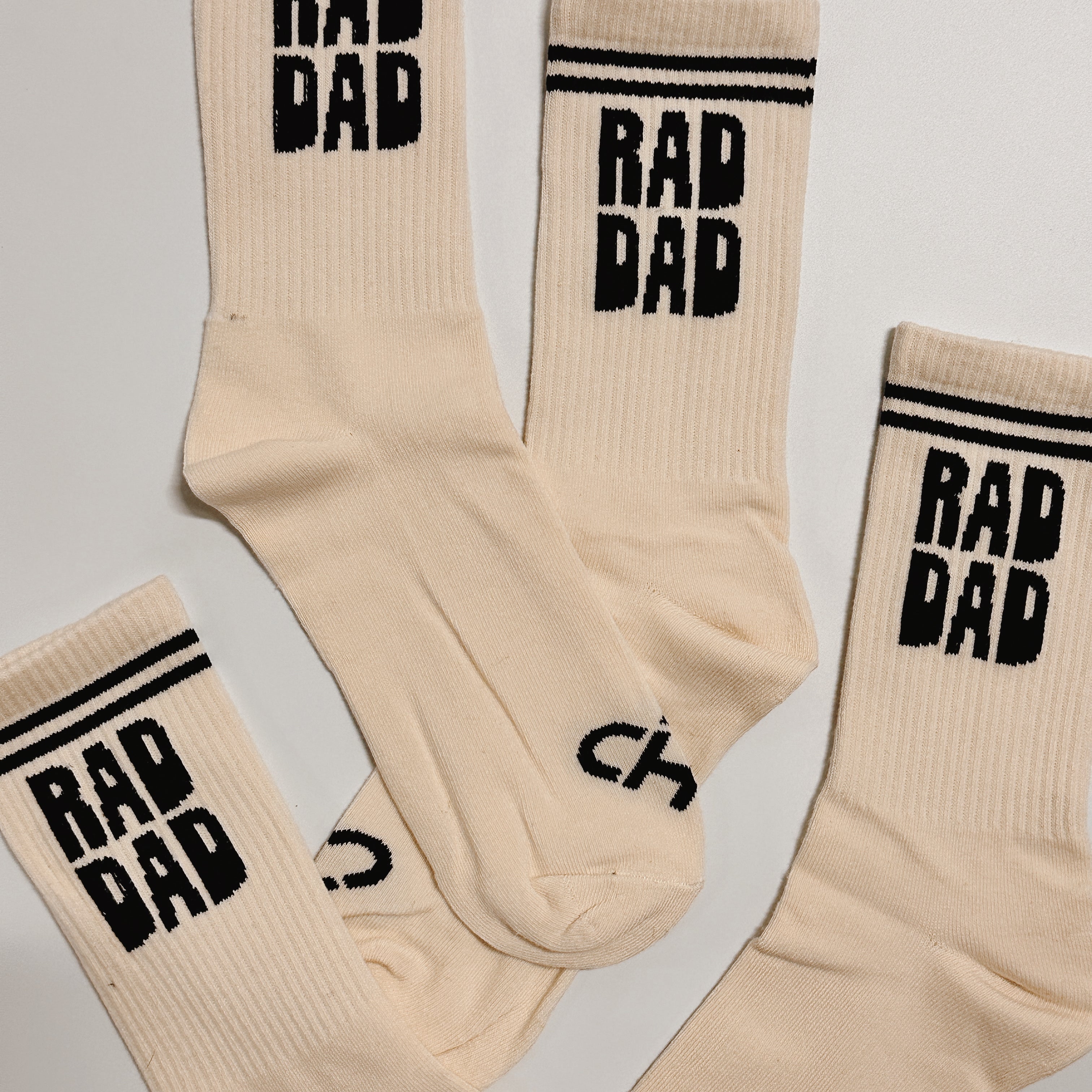 Rad Dad Socks, cream crew socks with black striped cuffs and bold black Rad Dad lettering, several laid flat