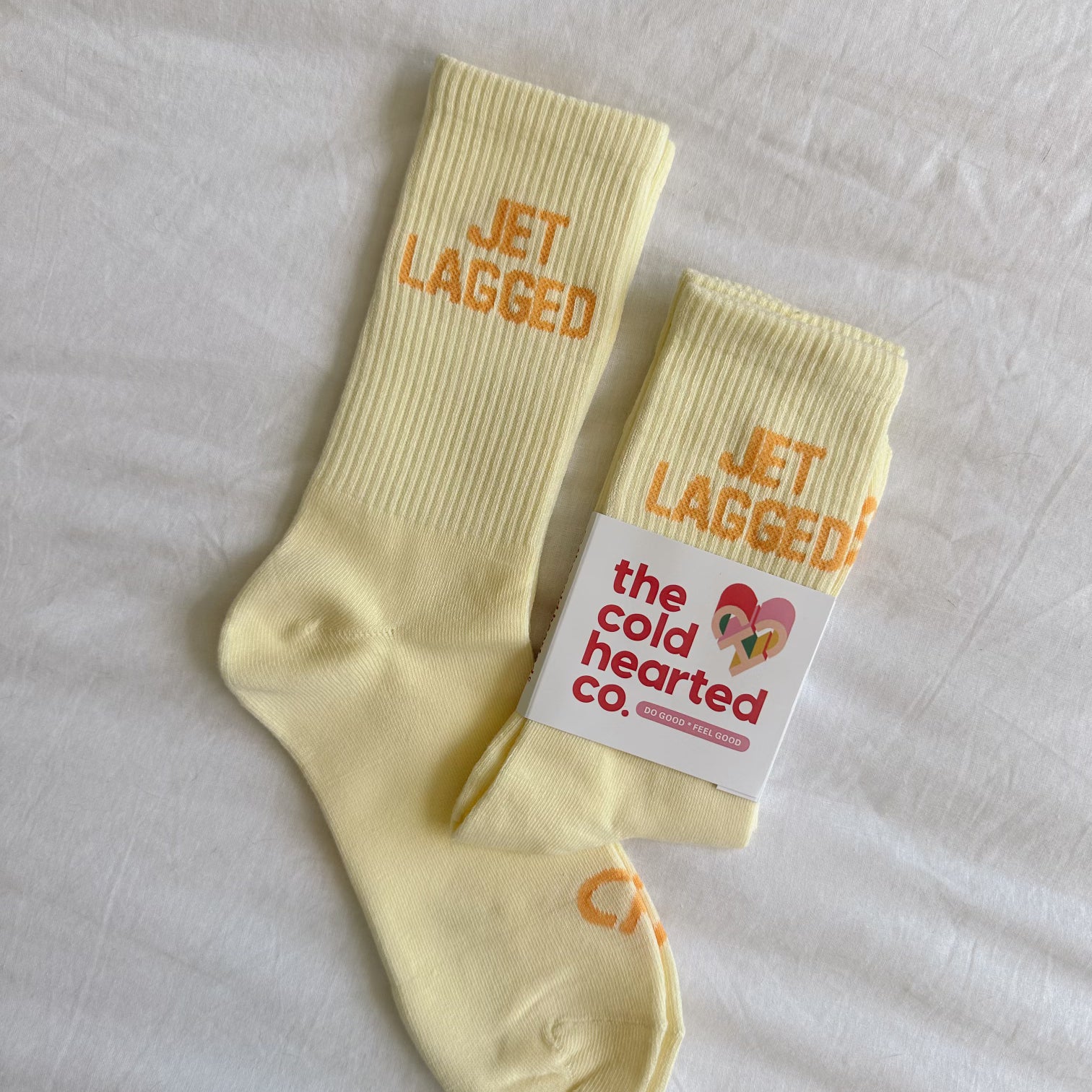 Jet Lagged Socks, pale yellow ribbed crew socks with orange Jet Lagged text and The Cold Hearted Co. band on white