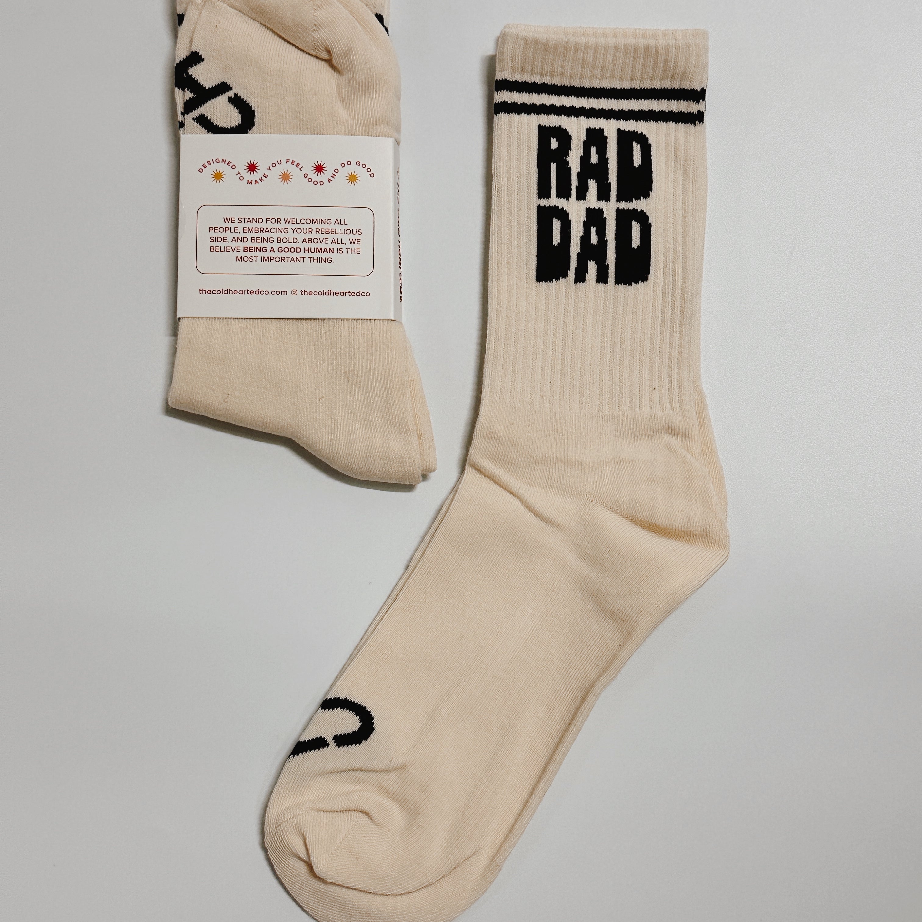 Rad Dad Socks, cream crew sock with black striped cuff and Rad Dad lettering beside a pair in a packaging band