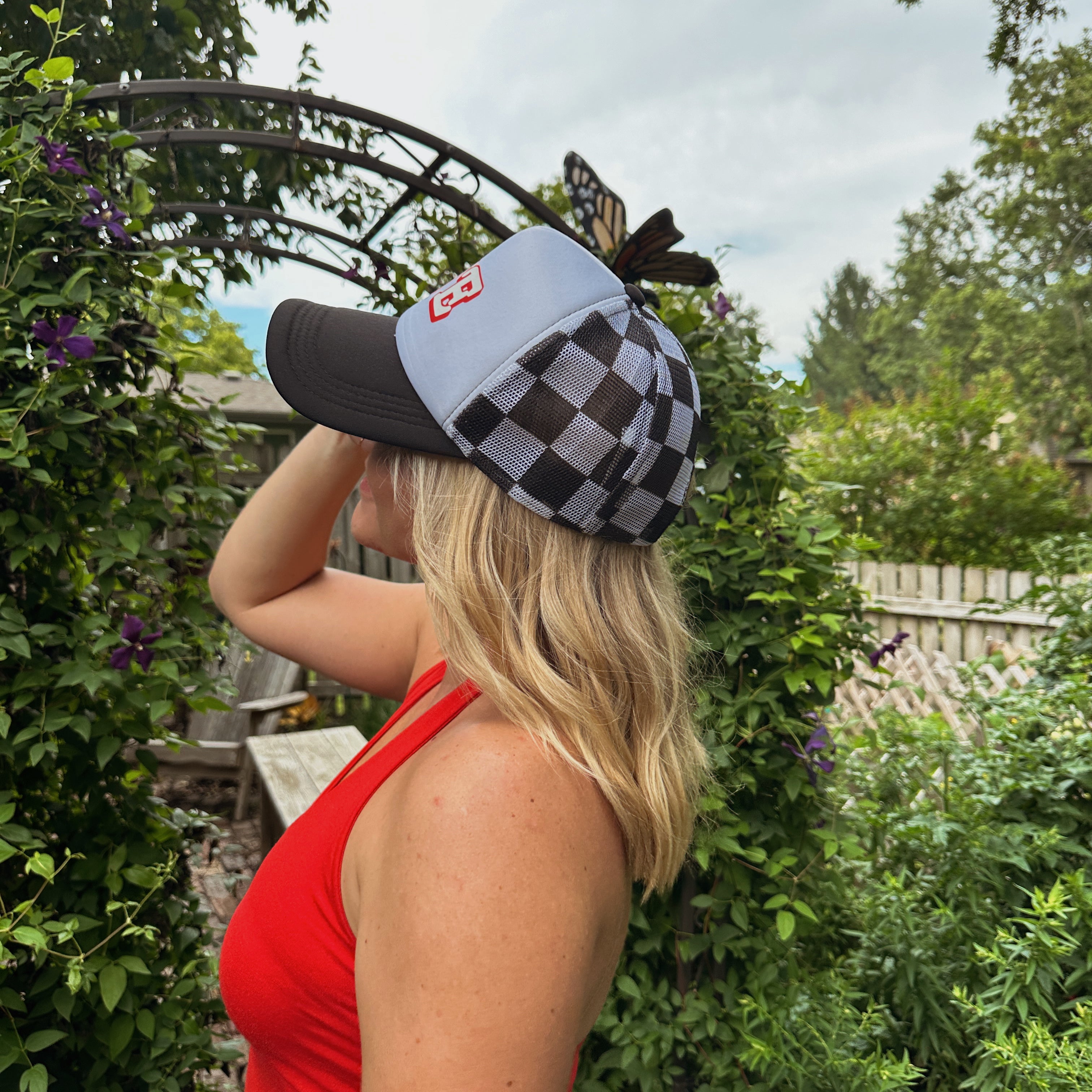 NE Checkered Trucker Hat worn by a blonde model in a red tank top, side view of black and white checkered mesh