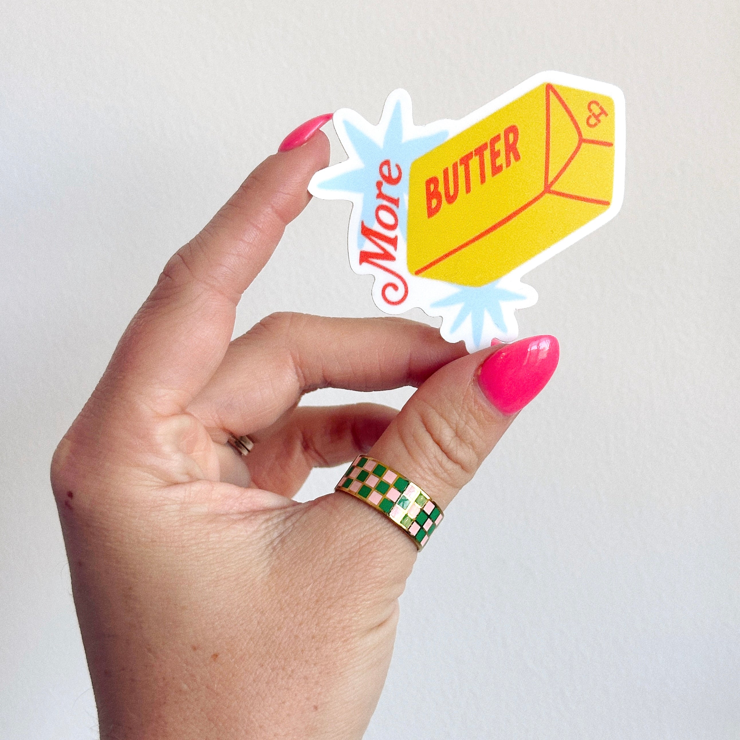 More Butter Sticker, yellow stick of butter reading More Butter with red script and blue burst, held in a hand