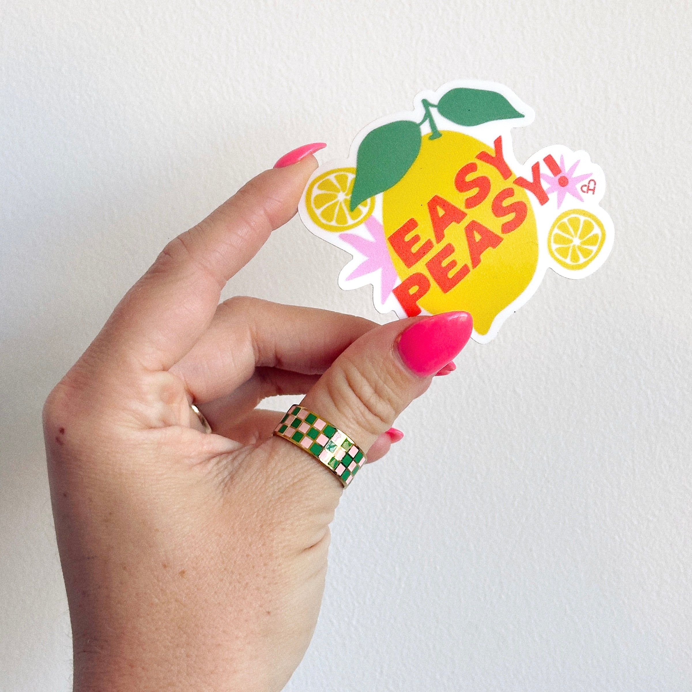 Easy Peasy Sticker, yellow lemon with green leaf and pink Easy Peasy lettering plus lemon slices, held in a hand