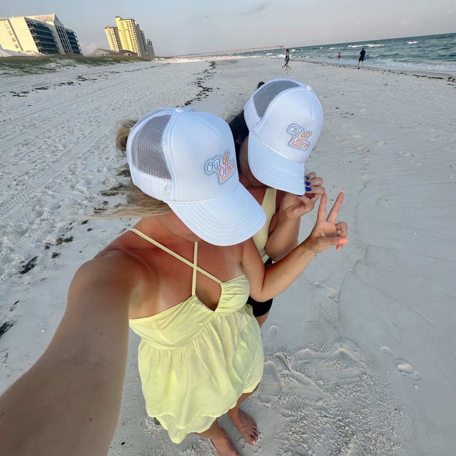 Out of Office Trucker Hat, two women in white trucker caps with Out of Office patches taking a selfie on the beach