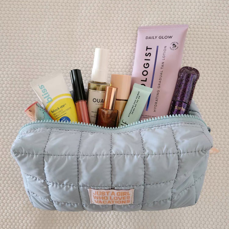Cosmetic Bag in light blue quilted nylon with Just A Girl Who Loves Vacations patch, filled with skincare and makeup