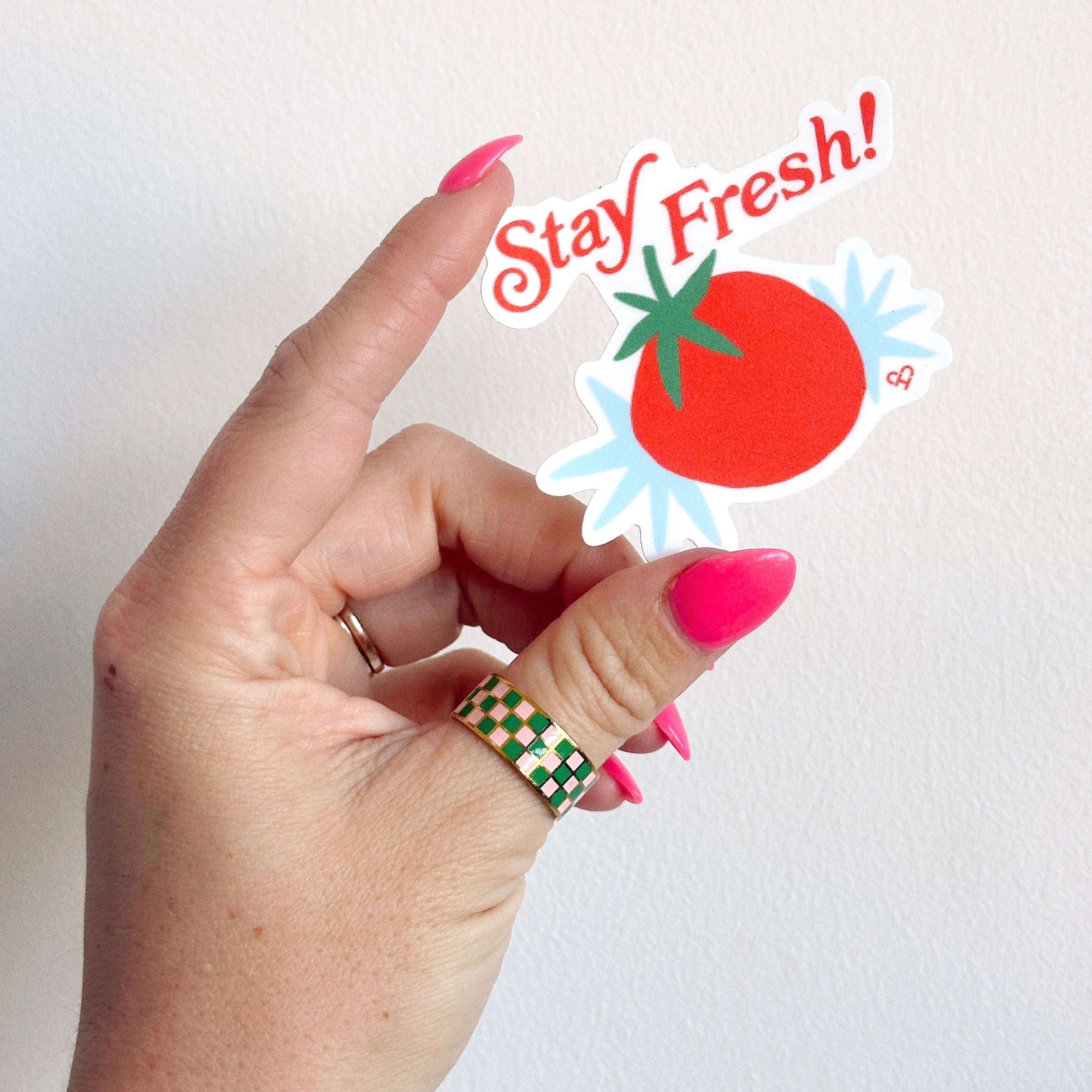 Stay Fresh Sticker, red tomato with blue burst and red Stay Fresh script, held up in a hand against a white wall