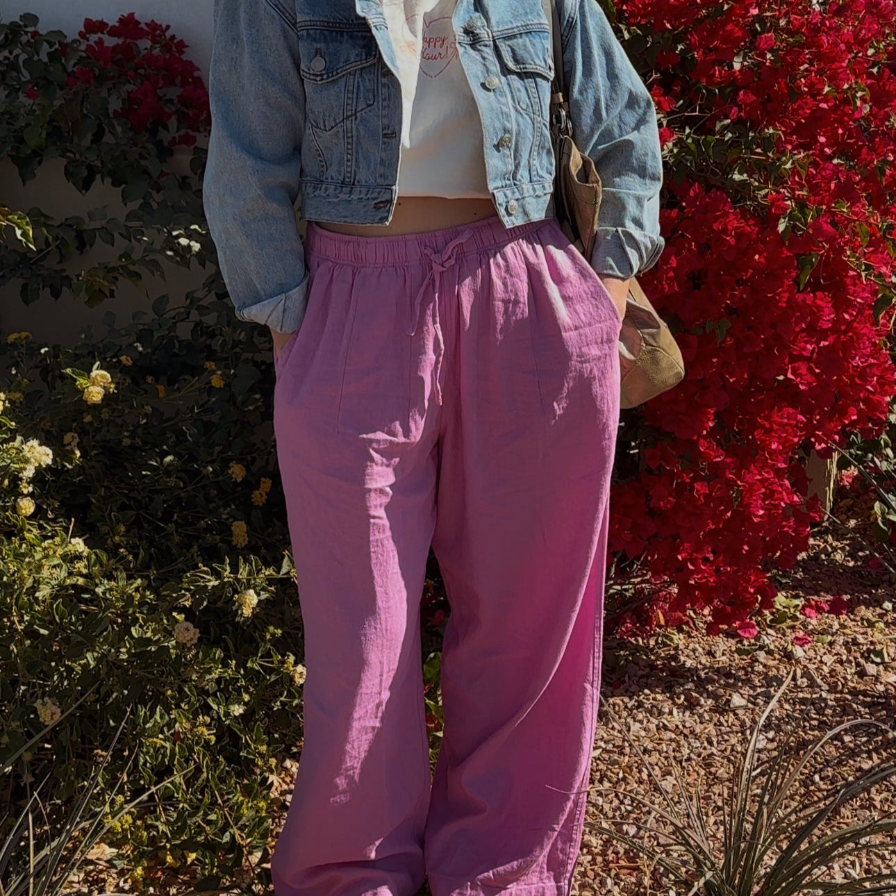 Yappy Hour Tee worn by a model with a denim jacket and pink pants in front of red bougainvillea