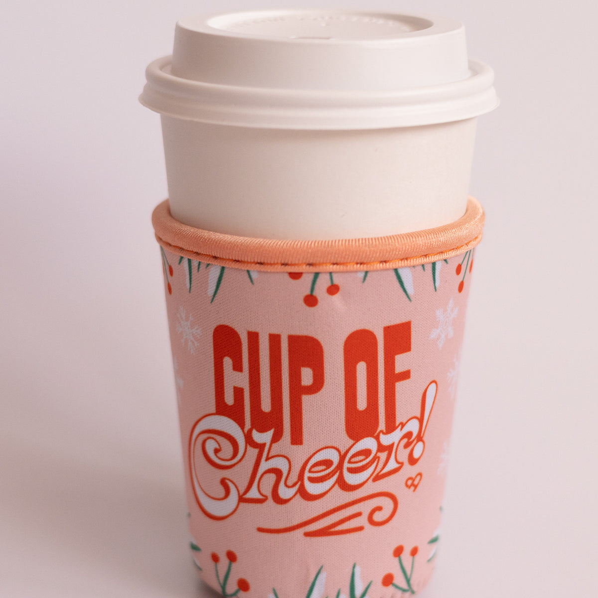 Cup of Cheer Coffee Koozie, pink holiday sleeve with red Cup of Cheer lettering and snowflakes on a white hot cup