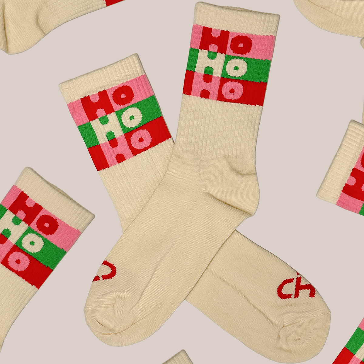 Ho Ho Ho Socks, cream crew socks with pink, red and green striped Ho Ho Ho bands, scattered flat lay on gray