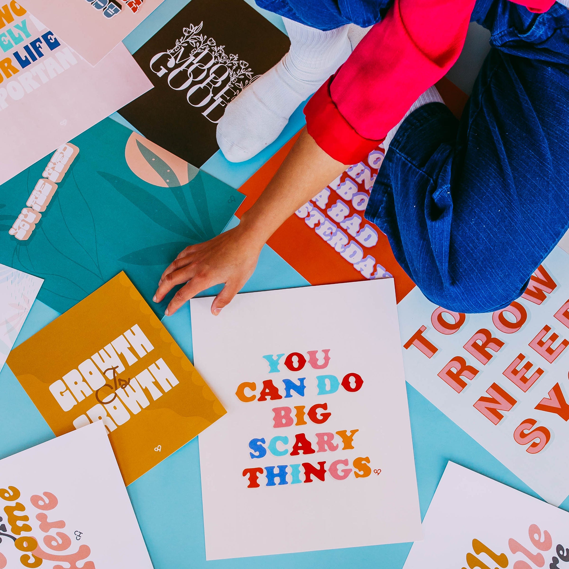 Surprise Print 5 Pack, assorted colorful typography prints spread on a teal floor around a seated model