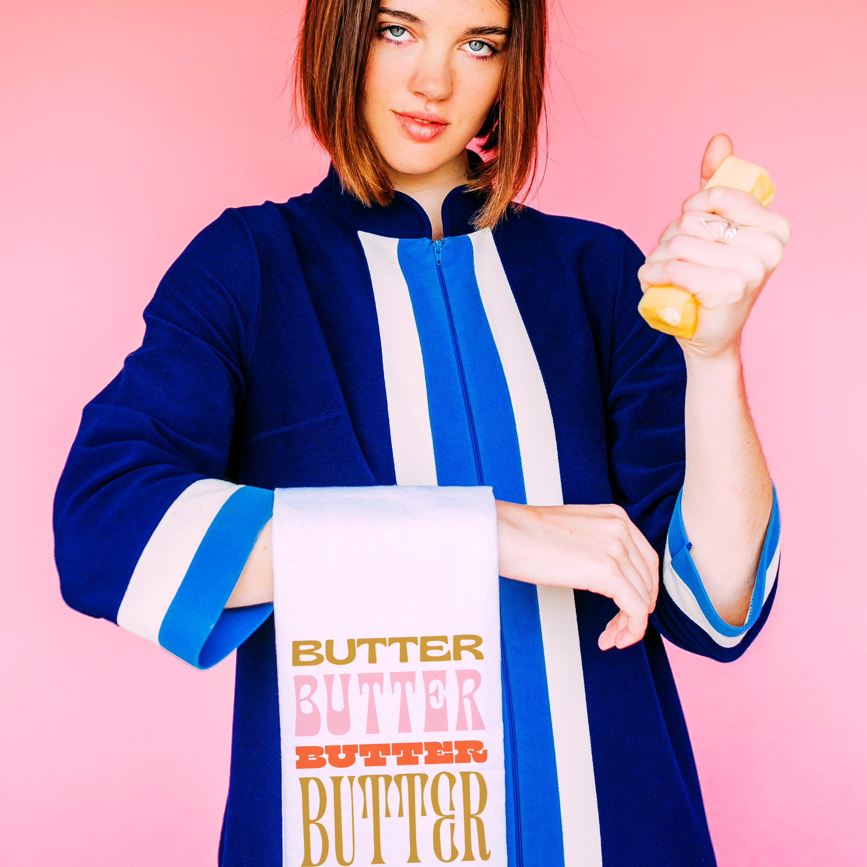 Butter Flour Sack Towel held by a model in a blue robe with a butter dish, repeating Butter text, pink wall